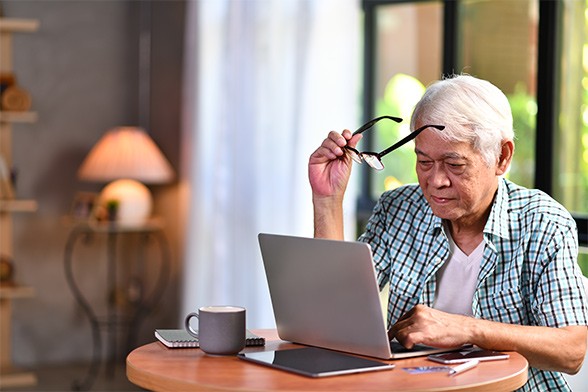 senior man putting glasses on to look at computer to research a fixed index annuity chicago il.